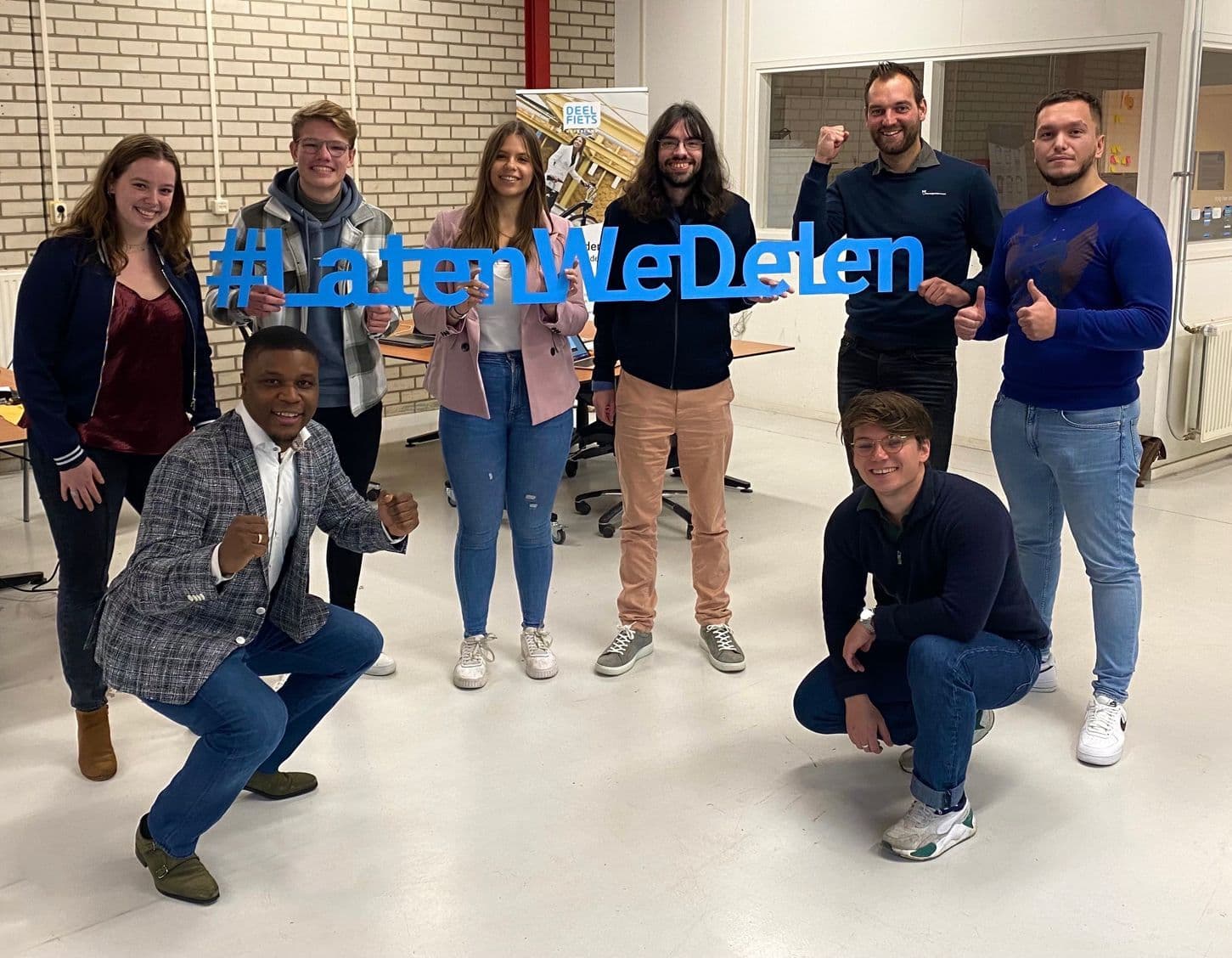 Het team van Deelfiets Nederland met een bord met de tekst "Laten we Delen"